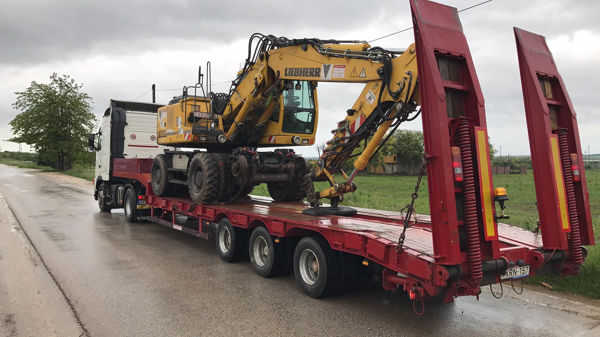 Liebherr forgókotró felrakva egy alvázas géptrailerre, esős úton